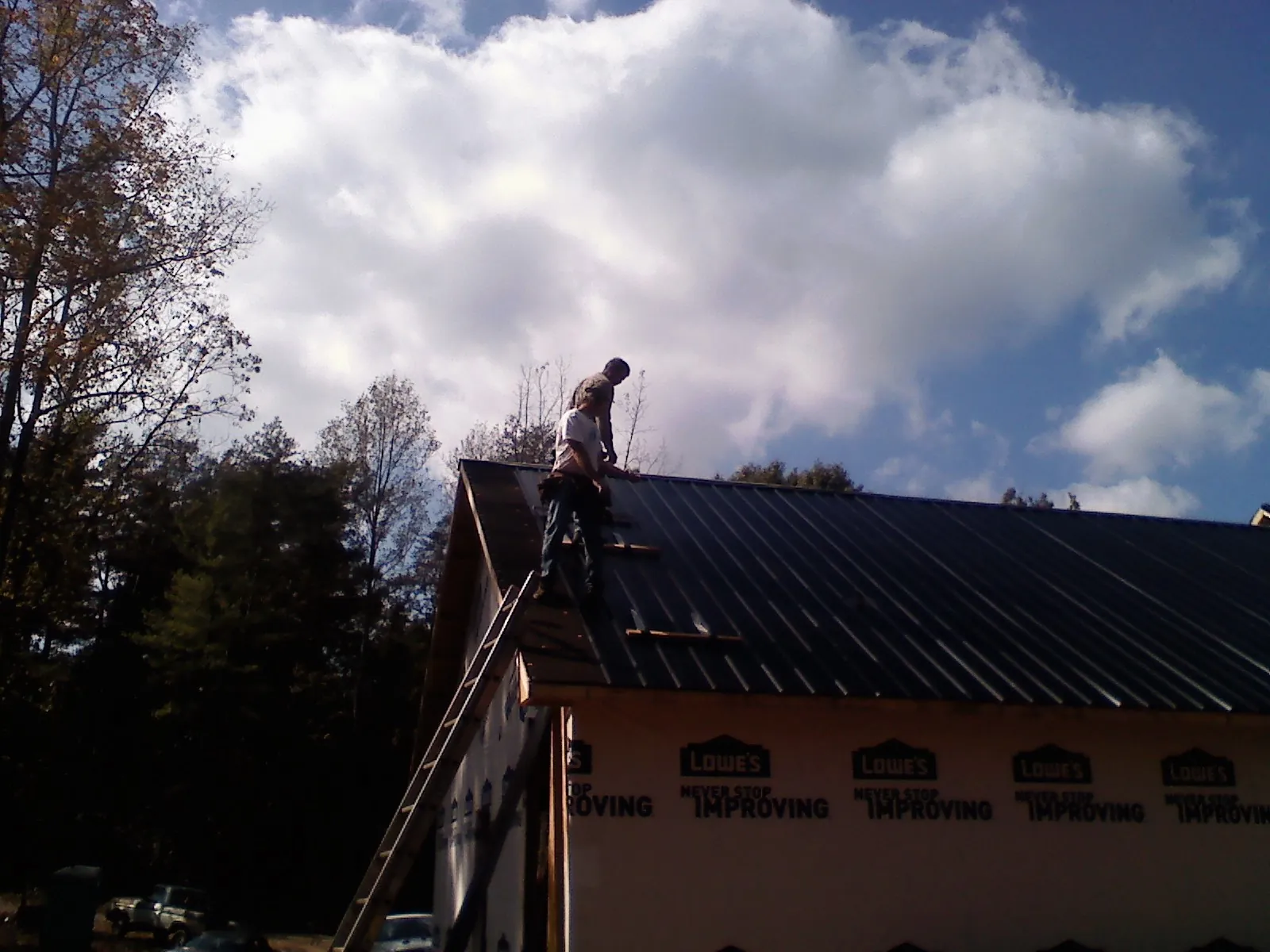 Roofer fastening dark metal panels high against a cloudy sky, from a Roof Inspection job in Plymouth